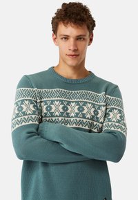 Teal knitted sweater with a white fair isle pattern across the chest and sleeves. Features a crew neck and ribbed cuffs.