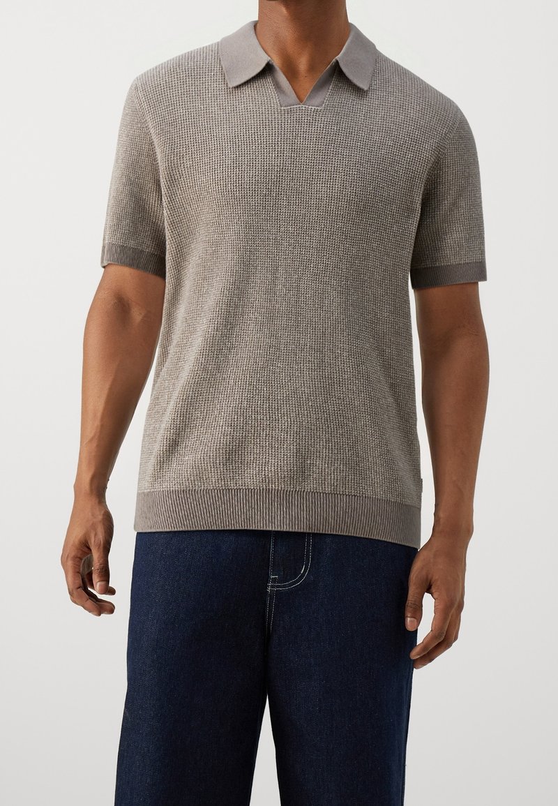 Krótki rękaw, jasnobrązowa koszulka polo z teksturowanym wzorem dzianiny, prążkowanym kołnierzykiem i mankietami, zestawiona z ciemnoniebieskimi spodniami dżinsowymi.