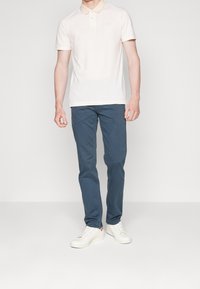 Ljust rosa polo skjorta med korta ärmar, kombinerad med marinblå byxor och vita sneakers. Har en klassisk krage och minimal branding.