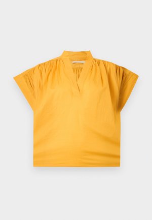 Blouse jaune à manches courtes avec un col en V, épaules froncées et un petit col montant, posée à plat sur un fond clair.
