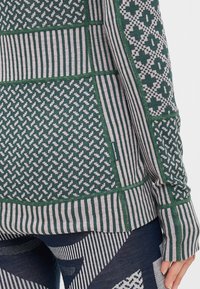 Langermet topp med en blanding av grønne og grå mønstre, inkludert striper og geometriske design, laget av et teksturert strikkemateriale.