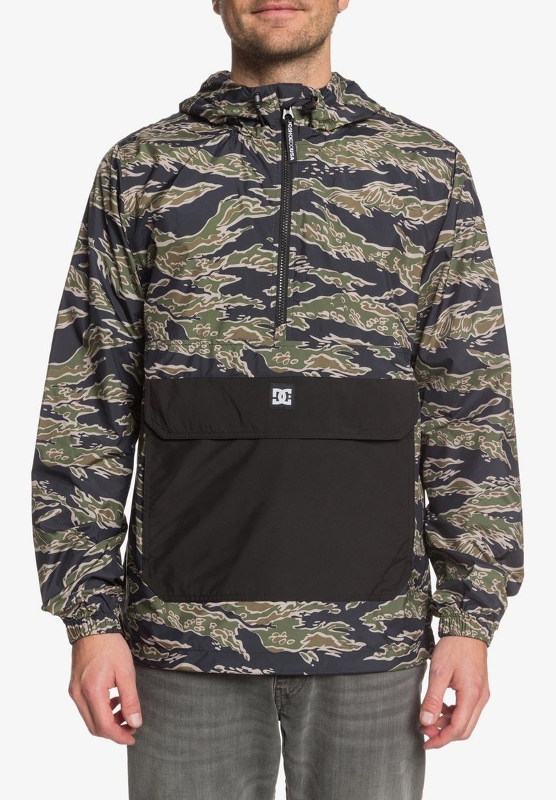 Lekka kurtka w kamuflażowym wzorze, wyposażona w czarną przednią kieszeń, regulowany kaptur oraz elastyczne mankiety. Wykonana z materiału syntetycznego.