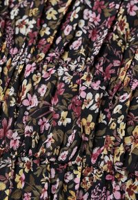 Robe fleurie en tissu léger, avec un fond noir et des motifs complexes de fleurs roses, jaunes et blanches, agrémentée de plis texturés.