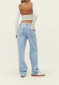 Vaqueros de tiro alto color azul claro, holgados, con textura desgastada y bolsillos traseros, combinados con una camiseta de crop top blanca de manga larga con un escote profundo en la espalda.