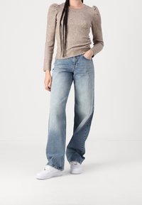Light brown ribbed long-sleeve top with puff sleeves paired with faded blue wide-leg jeans and white sneakers on a neutral background.