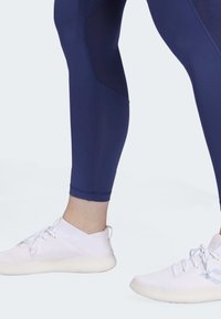 Námořnické legíny s texturovanými panely, kombinované s bílými sportovními botami s prodyšným svrškem a gumovou podrážkou, zobrazené od kotníku dolů.