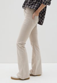 Beige flare jeans van katoen. Heeft een aangesloten taille, zijzakken en subtiele stiksels. Gecombineerd met witte sneakers.