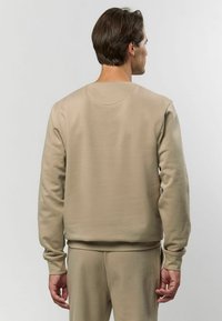 Sweatshirt bej cu guler rotund, manșete ribbate și o textură netedă. Are o croială lejeră și este asortat cu pantaloni de aceeași culoare.