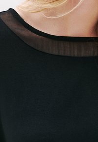 Schwarzes Oberteil mit einem runden Ausschnitt und einem transparenten schwarzen Überzug am Kragen; glatte Textur mit einem einfarbigen Körper.