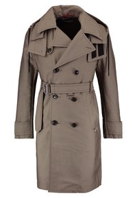 Trench-coat beige à double boutonnage avec larges revers, pattes d'épaule, boutons noirs, ceinture avec boucle et anneaux métalliques décoratifs.