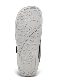 Suola di una scarpa per bambini con motivi esagonali testurizzati e una piccola faccia di scimmia sorridente in rilievo vicino al centro per aderenza e design.