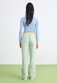 Camiseta ajustada de manga larga en azul claro combinada con pantalones holgados de color verde claro. Los pantalones tienen aberturas laterales y una cinturilla elástica.