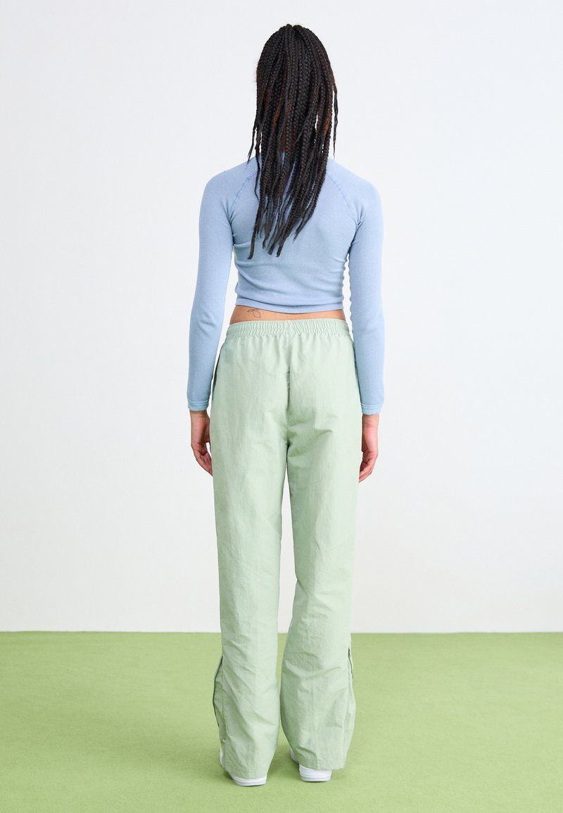 Camiseta ajustada de manga larga en azul claro combinada con pantalones holgados de color verde claro. Los pantalones tienen aberturas laterales y una cinturilla elástica.