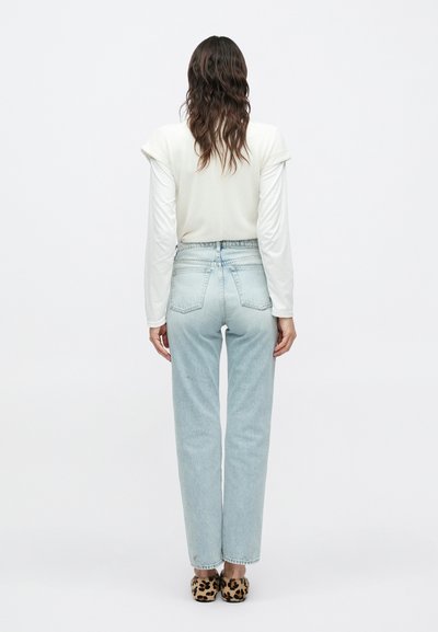 Ανοιχτό μπλε τζιν ψηλόμεσο με χαλαρή εφαρμογή, συνδυασμένο με ανοιχτό μπεζ μακρυμάνικη μπλούζα· το μοντέλο φοράει παπούτσια με λεοπάρ σχέδιο.