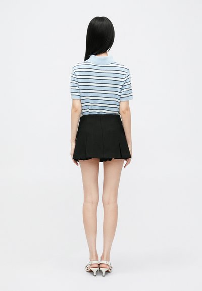 Hellblau gestreiftes Poloshirt, schwarzer plissierter Rock und hellfarbene Absätze. Glatte Texturen, lockeres Design und figurnahe Passform.