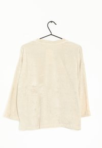 Camisa de manga larga beis con una textura suave y aterciopelada y un cuello redondeado, exhibida colgando sobre un fondo blanco.