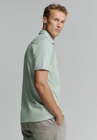 Lichtgroen polo-shirt met korte mouwen en een gladde textuur, met een kraag en opgerolde mouwen, gecombineerd met lichtgrijze shorts.