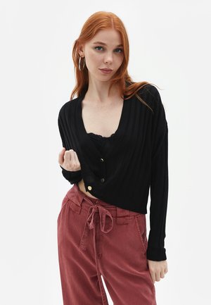 Sort ribbet langærmet cardigan med V-hals, der har tre knapper og et cropped design. Kombineret med højhased støvet lyserøde bukser.
