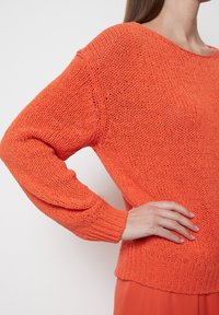 Sweter dzianinowy w jasnym pomarańczowym kolorze, o luźnym kroju, z prążkowanymi mankietami i szerokim dekoltem. Teksturowany materiał o swobodnym dopasowaniu.