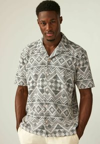 Camisa de botones de manga corta con un patrón geométrico en gris y blanco, hecha de una tela texturizada con un corte relajado y cuello.