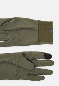 Gants vert olive avec une finition texturée, dotés d'un poignet ajusté, d'un accent noir au bout des doigts et de détails discrets en motif sur les paumes.