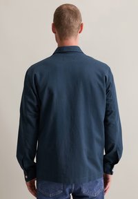 Donkerblauwe shirt met een rechte snit, lange mouwen en een kraag. De stof lijkt soepel, met knoopmanchetten en een losse pasvorm.