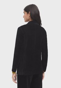 Veste en velours côtelé noire avec un col, des manches longues et une coupe droite. Présente une texture à côtes verticales et aucun matériel visible.