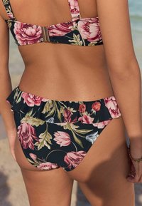 Costum de baie floral cu o bază neagră și modele de flori roz și verzi. Bustiera are bretele ajustabile și închidere cu clips; slipul are o margine volan.