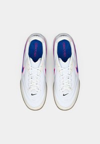 Λευκά αθλητικά παπούτσια με στρογγυλή μύτη, επικαλυμμένα με υφασμάτινο δέρμα, μαύρο λογότυπο Nike και φωτεινές ροζ λεπτομέρειες στο πλάι και την φτέρνα. Μπλε εσωτερική σόλα.