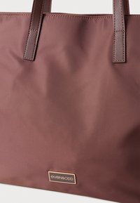 Saco de mão castanho com duas alças de pele cosidas e uma pequena placa retangular de metal com a inscrição "even&odd."