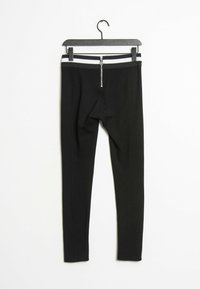 Zwarte leggings met een aansluitend ontwerp, voorzien van een elastische tailleband met zwart-witte strepen en een frontale rits. Gladde stoftextuur.
