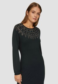 Langärmliges schwarzes Kleid mit einem runden Ausschnitt und einem aufwendigen, mit Perlen verzierten geometrischen Muster um den Kragen. Weicher, strukturierten Stoff.