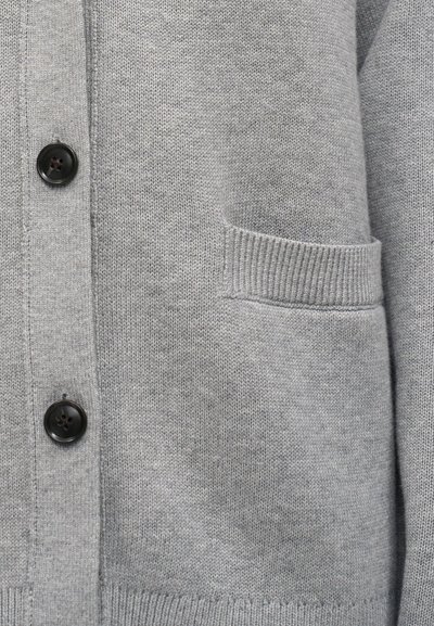 Γκρι πλεκτή ζακέτα με μαύρα κουμπιά και μια μικρή ανοιχτή τσέπη στη δεξιά πλευρά, που δείχνει λεπτομερή υφή υφάσματος.