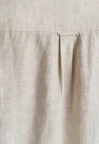 Tejido de lino beige con una textura sutil, con un detalle de pliegue cerca de la parte superior y una línea de costura a lo largo del borde superior.