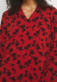 Vestido de estampado floral rojo con un patrón de flores negras, escote en v y tela fluida con mangas largas.