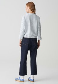 Hellblauer, strukturierter Pullover mit Dreiviertelärmeln, kombiniert mit dunkelblauen, weit geschnittenen Jeans und blauen Sportschuhe.