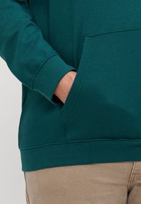 Felpa color teal con maniche lunghe e tasca frontale. Presenta polsini e orlo a costine, realizzata in un morbido tessuto misto cotone.