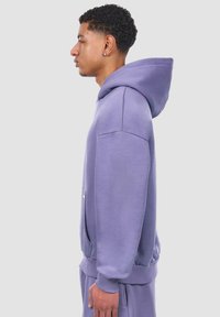 Helllila Kapuzenpullover mit einer vorderen Tasche, gerippten Bündchen und einer lockeren Passform. Glatte Textur und sichtbare Nähte.