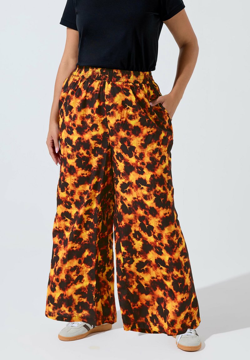 Breda byxor i ett livligt, eldig mönster av orange, gult och svart. Tillverkade av lätt material med resårmidja och sidfickor.