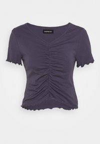 Lila kortärmad topp med v-ringning, med samlade detaljer fram och scallopade kanter på ärmar och nederkant. Mjuk tygtextur.