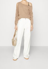 Top marrón de manga larga con diseño de hombros descubiertos, combinado con pantalones blancos sueltos. El conjunto incluye un bolso beige con correa para el hombro y zapatos blancos.