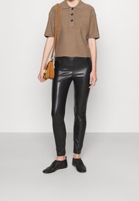 Brun kortärmad pikétröja med tre svarta knappar, kombinerad med glänsande svarta leggings och svarta mjuka läderskor. Brun axelväska ingår.