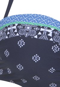 Bikini-Oberteil mit navyfarbenem Grund, weißen geometrischen Mustern, blauem Band und grünen Akzenten. Hergestellt aus glattem, dehnbarem Stoff.