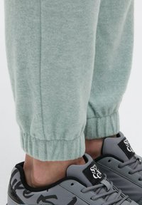 Hellgrüne Fleece-Jogginghosen mit elastischen Bündchen, kombiniert mit grauen Sneakern mit schwarzen Akzenten und einem Logo auf der Zunge.