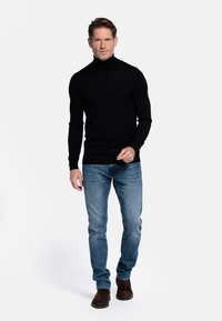 Zwarte coltrui met lange mouwen en een getailleerd ontwerp, gecombineerd met lichtblauwe jeans en bruine suède enkellaarsjes.