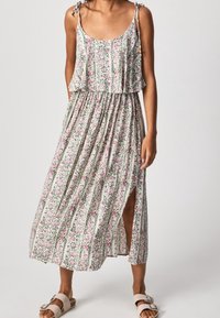 Bloemen maxi-jurk met een gelaagd ontwerp, spaghettibandjes en een zijsplit. Heeft roze en groene patronen op een lichte achtergrond.