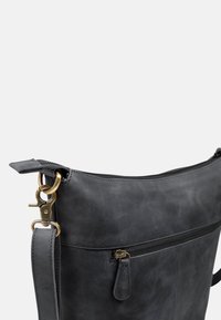 Black leather shoulder bag with a zippered pocket, brass hardware, adjustable strap, and smooth texture. Features a minimalist design.