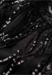 Gros plan sur un tissu noir avec des paillettes noires brillantes disposées en motifs ondulés sur un fond en résille.