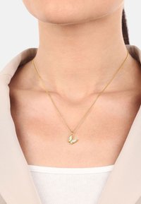 Collana d'oro con ciondolo a forma di farfalla, dotata di inserti verde chiaro e una catena sottile, indossata su uno sfondo neutro.