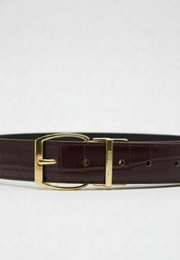 Brązowy skórzany pasek z wzorem krokodyla, z metalową klamrą w złotym odcieniu oraz charakterystycznym logo w pobliżu klamry.